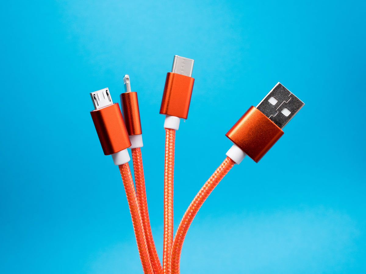 Orange charging cables with USB-A, USB-C, Micro-USB, and Lightning connectors against a bright blue background.