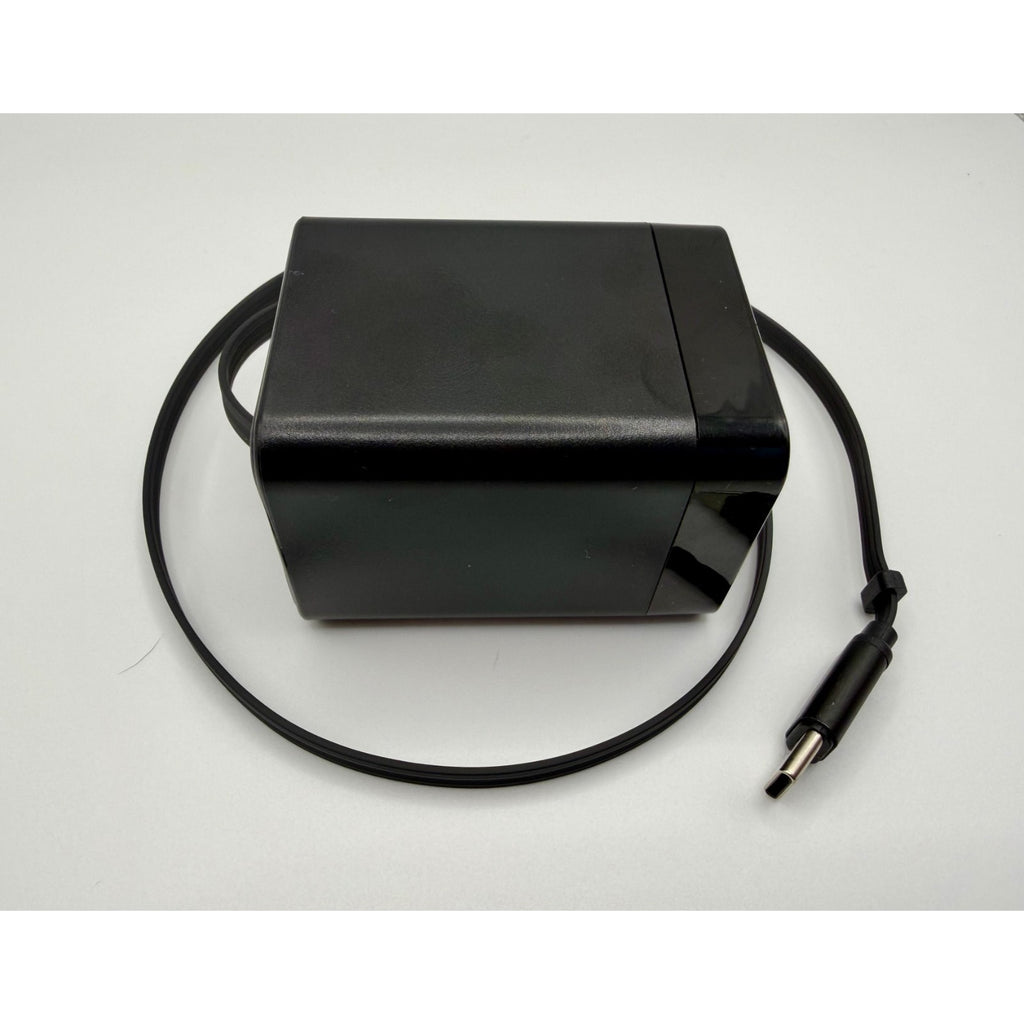 A 65W GaN USB-C Wall Charger with built-in cable and foldable plug, in black, is placed on a white surface.