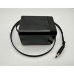 A 65W GaN USB-C Wall Charger with built-in cable and foldable plug, in black, is placed on a white surface.
