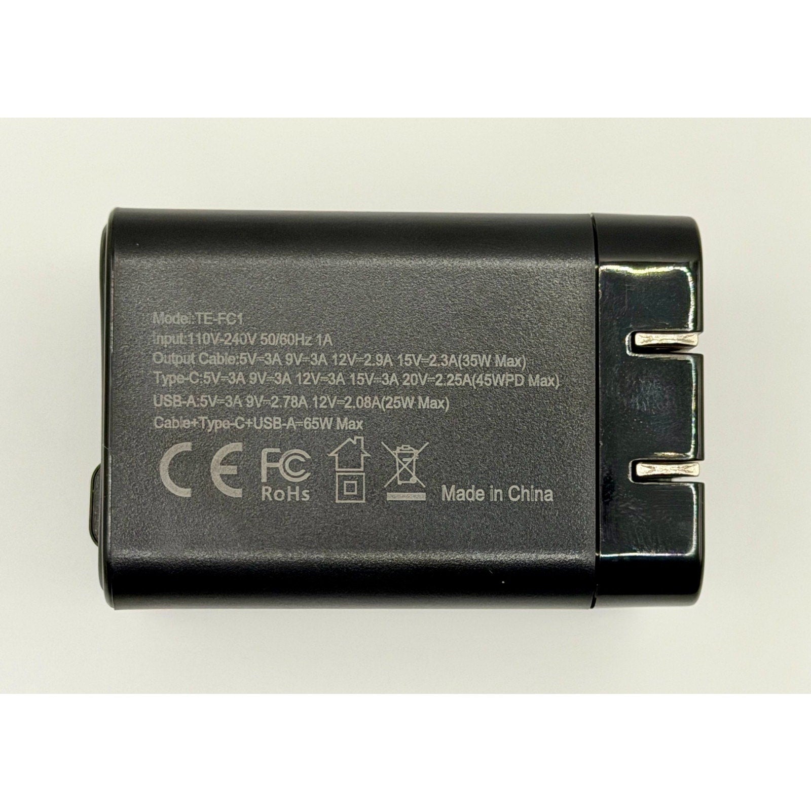 The 65W GaN USB-C Charger PD Fast Charge features a foldable plug, built-in cable, black finish with white specs, fast charging via USB and Type-C compatibility, input/output voltage info, and certification logos. Brand new.