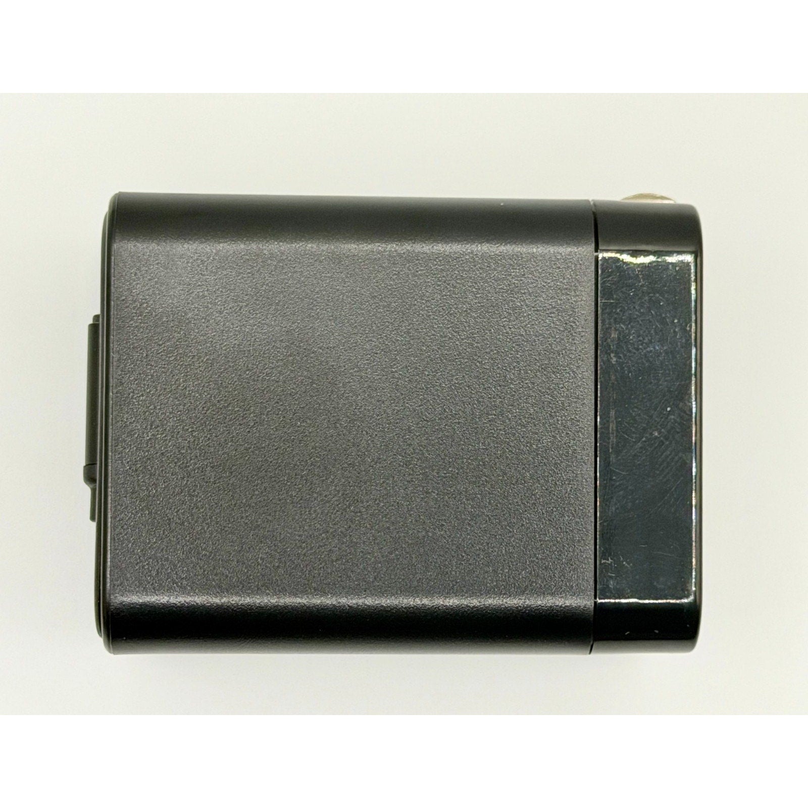 A black, rectangular 65W GaN USB-C Wall Charger with built-in cable and foldable plug features a slightly worn, shiny area on one end and is photographed against a plain white background.