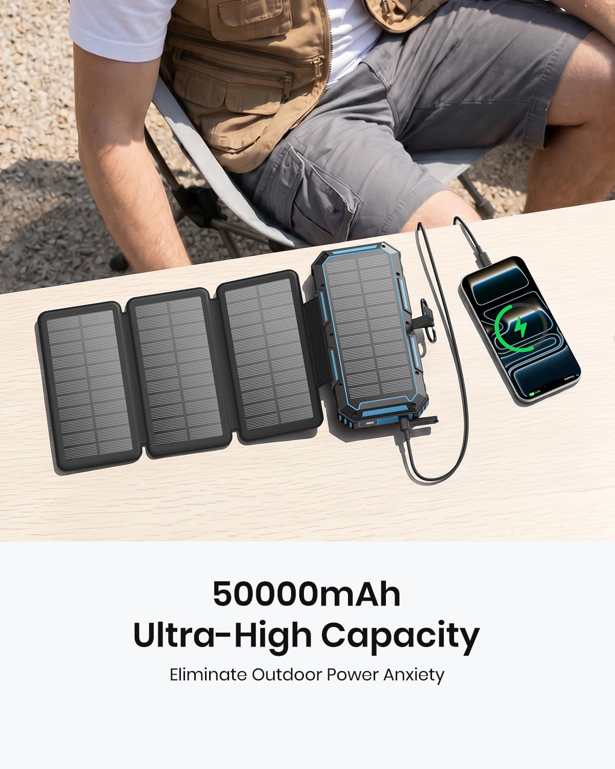 A person sits outdoors beside a table holding the 50000mAh Solar Power Bank – Magnetic Wireless Charger with Hand Crank, 4 Solar Panels & Built-In Charging Cables, as it charges a smartphone. This foldable solar charger eliminates outdoor power anxiety, offering an emergency power bank solution for all your adventures. The image text highlights its ultra-high capacity and dependable charging wherever you go.