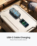A person relaxes on a bench outdoors, effortlessly charging their iPhone 17 with the 50000mAh Solar Power Bank – Magnetic Wireless Charger featuring hand crank, four solar panels, and built-in charging cables. Text reads: "USB-C Cable Charging. iPhone 17 from 0 to 60% in 30mins." The power bank sits conveniently on a cooler nearby, showcasing its reliable emergency power capabilities.