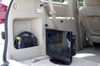 A Naxa 12 Volt DC Cord powers a portable DVD player in the back of a car via the cigarette lighter socket, with a car tool kit in a side compartment and a seatbelt hanging nearby.