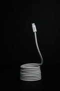 The Luxe Magnetic Cable, a coiled gray USB-C cable with a visible connector, stands upright against a black background—its heavy-duty build is perfect for fast charging.
