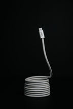 The Luxe Magnetic Cable, a coiled gray USB-C cable with a visible connector, stands upright against a black background—its heavy-duty build is perfect for fast charging.