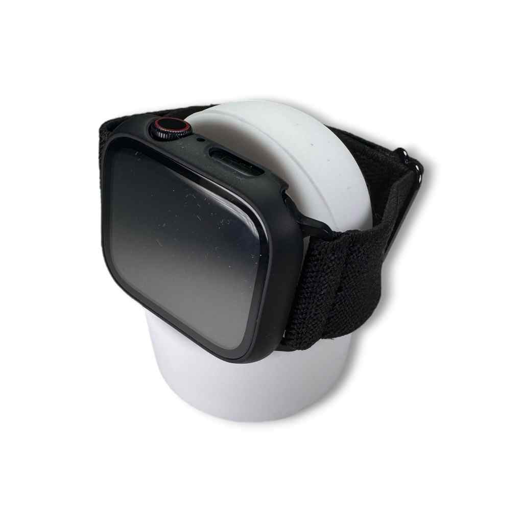 A black smartwatch with a fabric strap sits on a Charging Stand, elegantly displayed on a cylindrical surface against a white background.