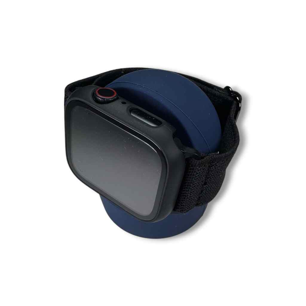 A black smartwatch with a black band rests on a dark blue circular silicone Charging Stand against a white background.