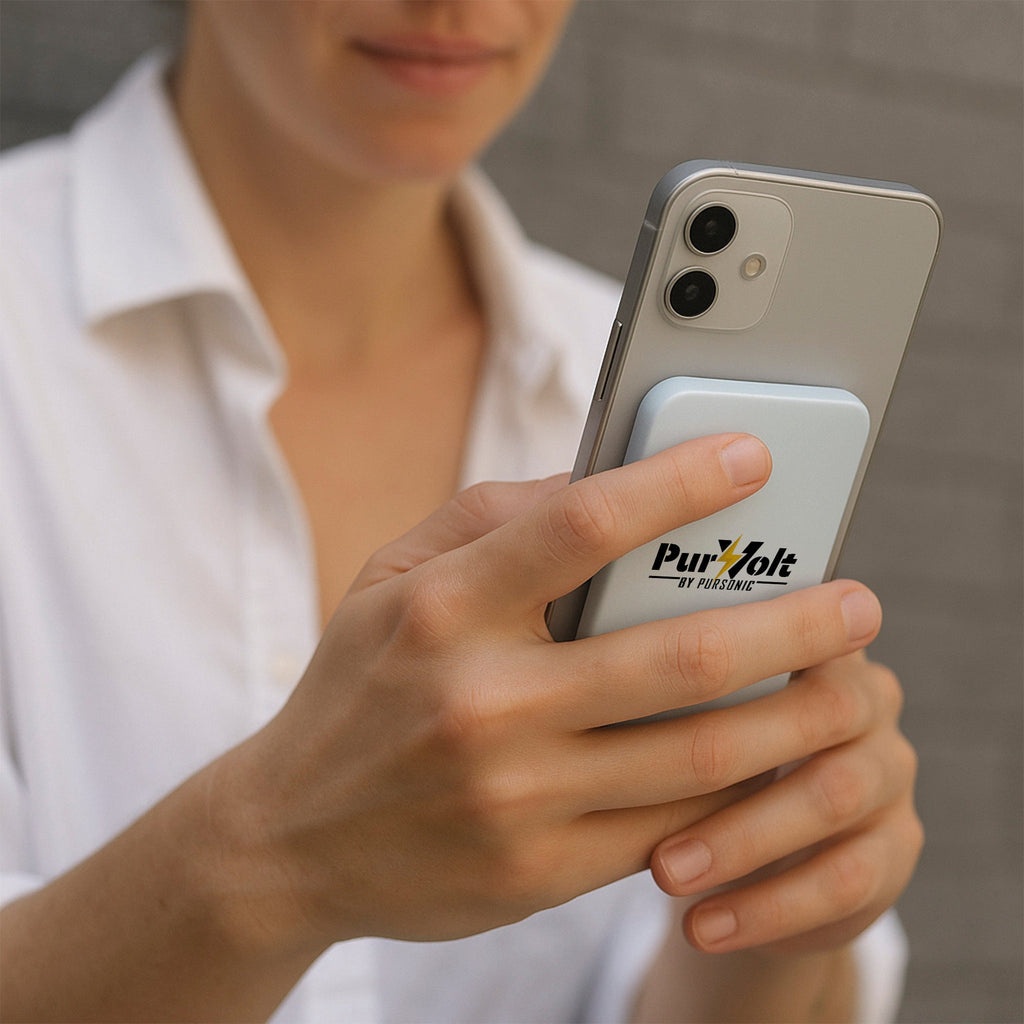 A person in a white shirt holds a smartphone with a Pursonic Ultra-Compact 5000mAh Wireless Power Bank attached to the back, standing against a gray background.
