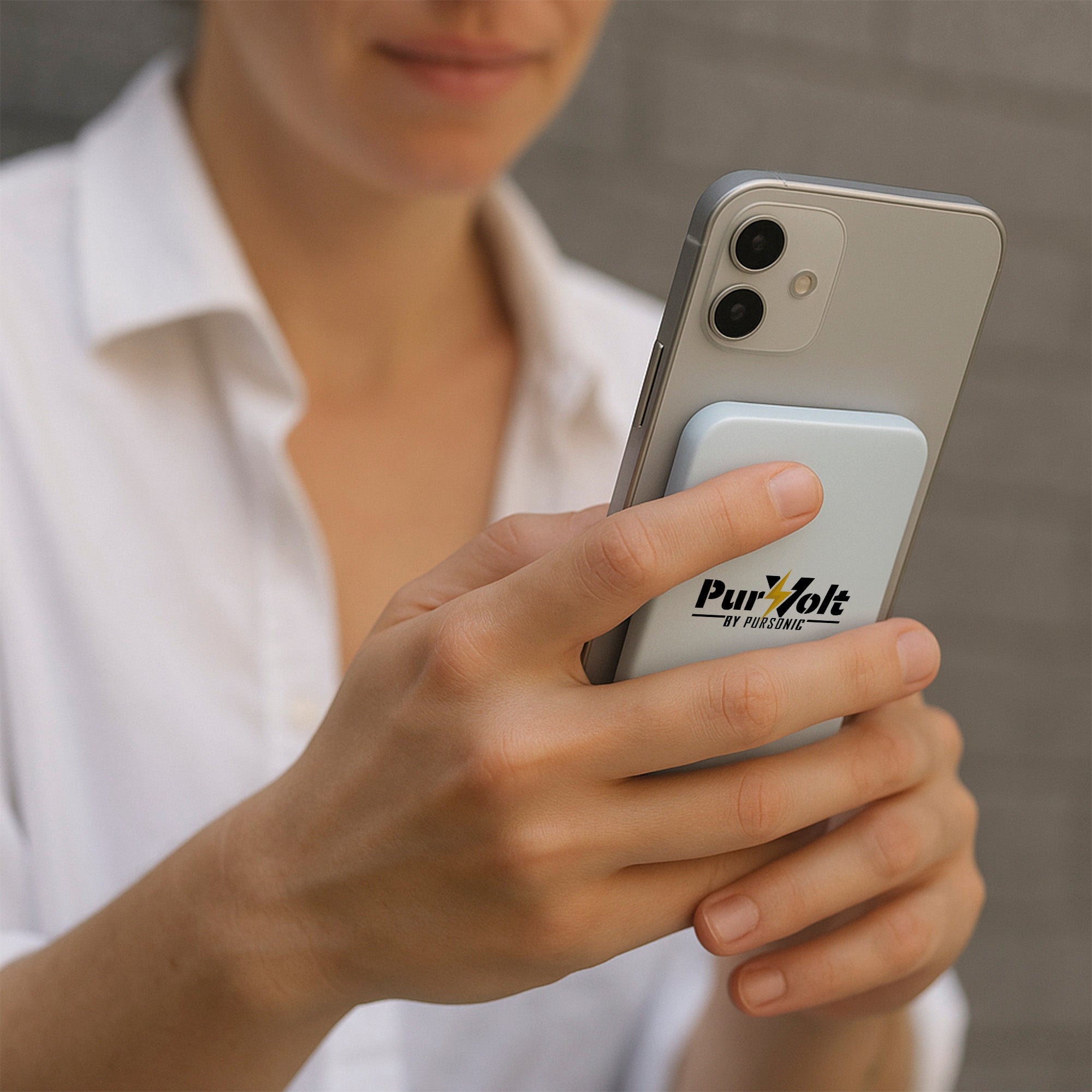 A person in a white shirt holds a smartphone with a Pursonic Ultra-Compact 5000mAh Wireless Power Bank attached to the back, standing against a gray background.