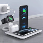 A wireless charging station on a desk charges a smartphone, smartwatch, and wireless earbuds while another phone is propped upright, all devices connected to a wall outlet.
