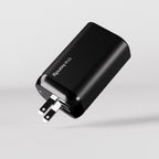 A black wall charger called "The Fast Charger" with two metal prongs and two USB ports is shown against a plain, light gray background.
