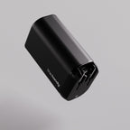 A black rectangular electronic device with two prongs, resembling a power adapter, labeled "The Fast Charger" on its side, set against a plain light gray background.