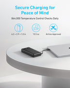 The Anker Power Bank (20K, 87W, Built-In USB-C Cable) charges a laptop on a white round table. Enjoy secure charging with daily temperature checks, compact and lightweight design, airline approval, and fast USB-C charging capability.