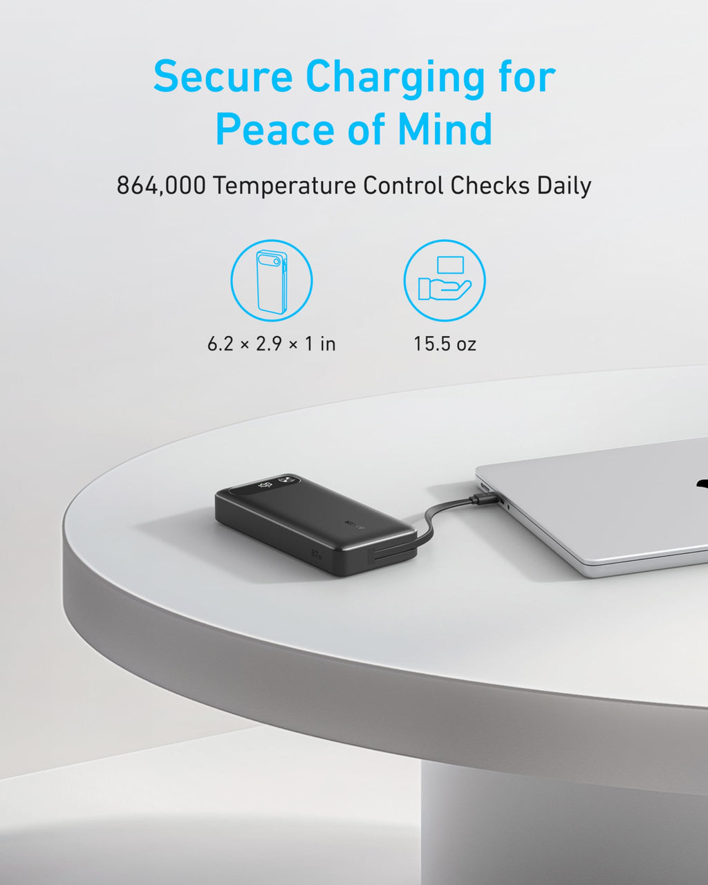 A black Anker Power Bank (20K, 87W, Built-In USB-C Cable) charges a silver laptop on a white round table. Secure USB-C fast charging, 20000mAh capacity, 864,000 daily temperature checks; size: 6.2×2.9×1 in; 15.5 oz.