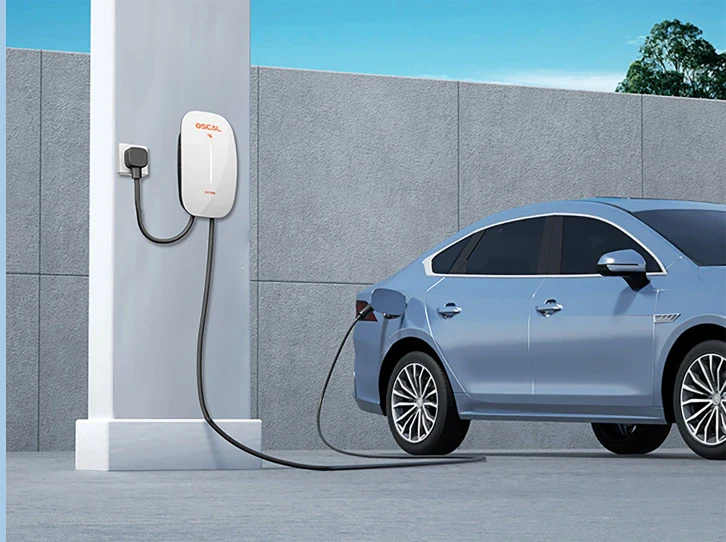 A blue electric car is parked and charging outdoors using the EV Charger 7kw, a smart wall-mounted unit with a cable plugged into the car near the rear wheel.