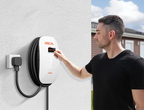 A man in a black shirt uses the EV Charger 7kw, its cable coiled neatly. This smart wall-mounted Level 2 charger, plugged into an outdoor socket, provides convenient home charging outside the house.