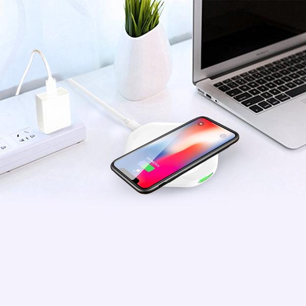 An Esoulk QI Certified 10W Wireless Charging Fast Charger Pad charges a smartphone wirelessly beside a silver laptop and potted plant on a clean, white desk—perfect inspiration to explore more styles for your workspace.