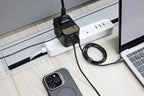 A modern, organized desk setup features a power strip with multiple devices plugged in, including the 65W GaN Travel Adapter, various chargers and cables, plus a laptop and smartphone placed nearby.